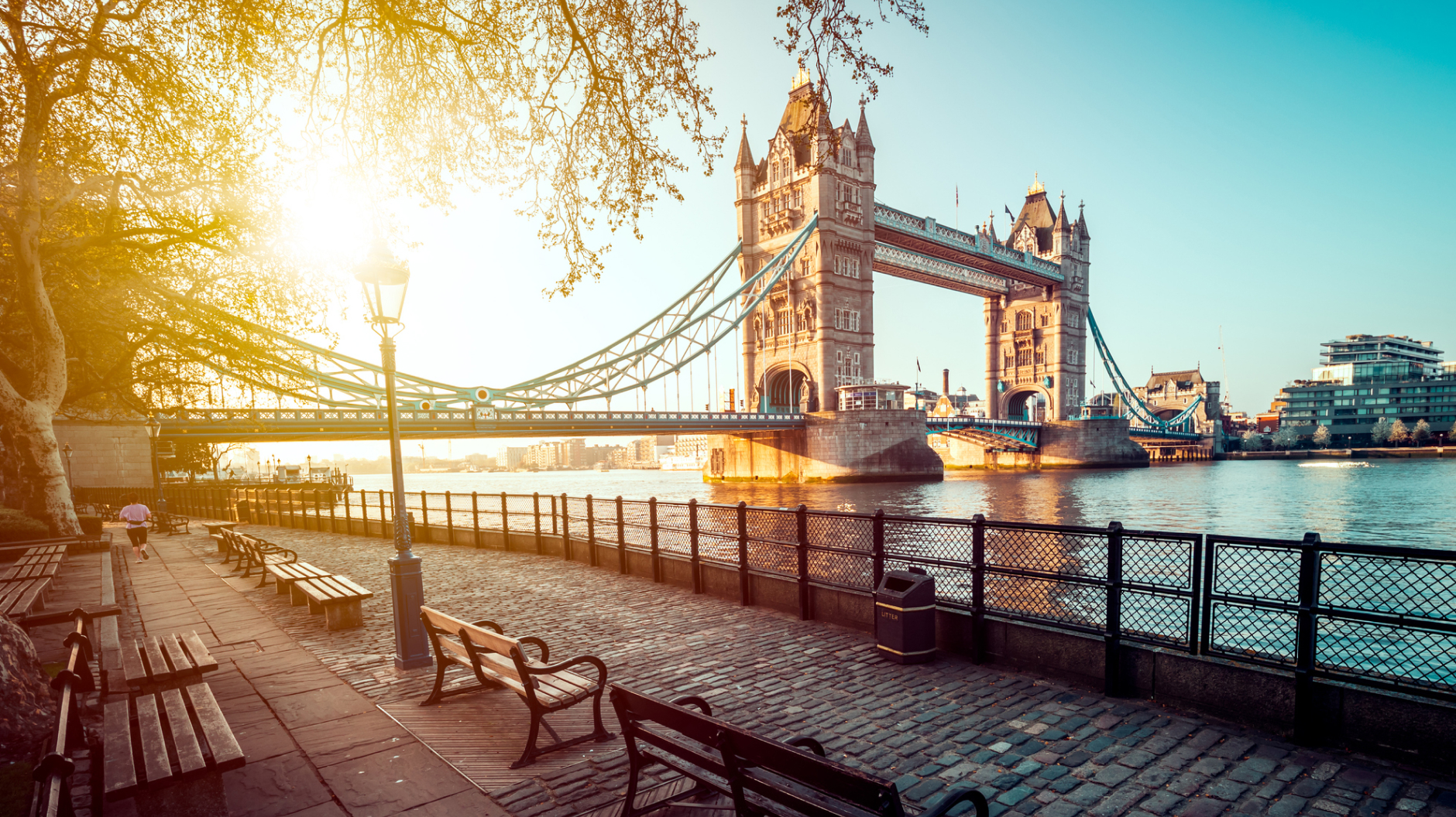 A picture of Tower Bridge in London with blue sky and the sun shining through nearby trees